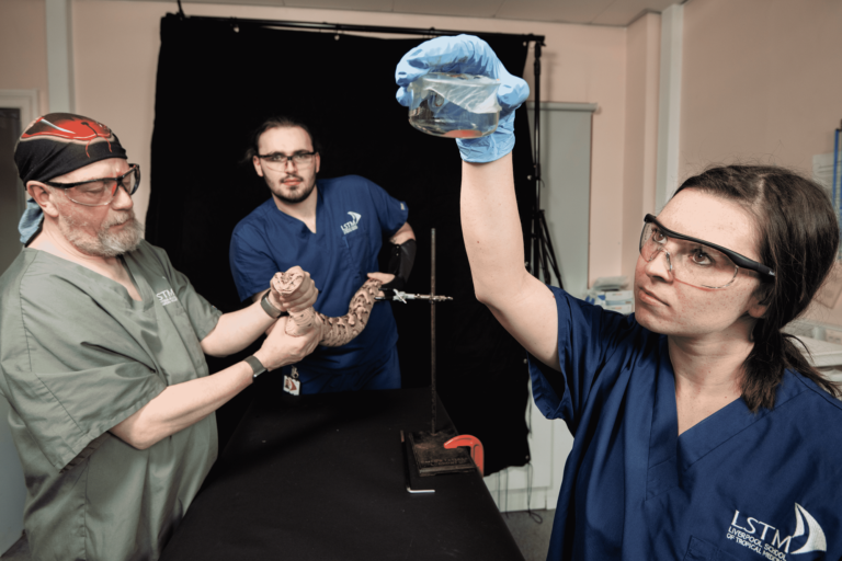 Wearing LSTM scrubs, Becky Edge holds a small jar of venom, while Paul Rowley and Edd Crittenden hold a Puff Adder.
